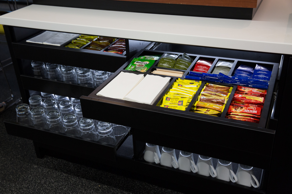 Multiple drawers in workplace kitchen hub with organisers for various pantry consumables and crockery