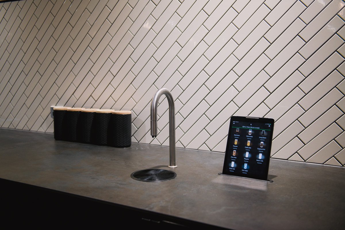 A TopBrewer coffee machine and iPad against a dark counter and white tiled walls