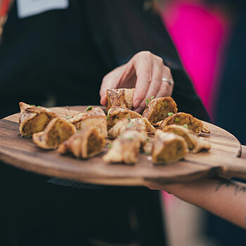 Person picking up an appetiser laid out on a wooden board being held by a caterer